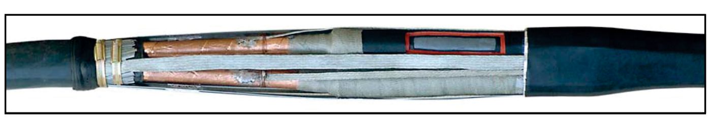 A finished three-core straight-through joint with its outer sleeve cut back, showing the copper-screened cores, the grey wraparound joint case and the black outer jacketing sleeve over the cable